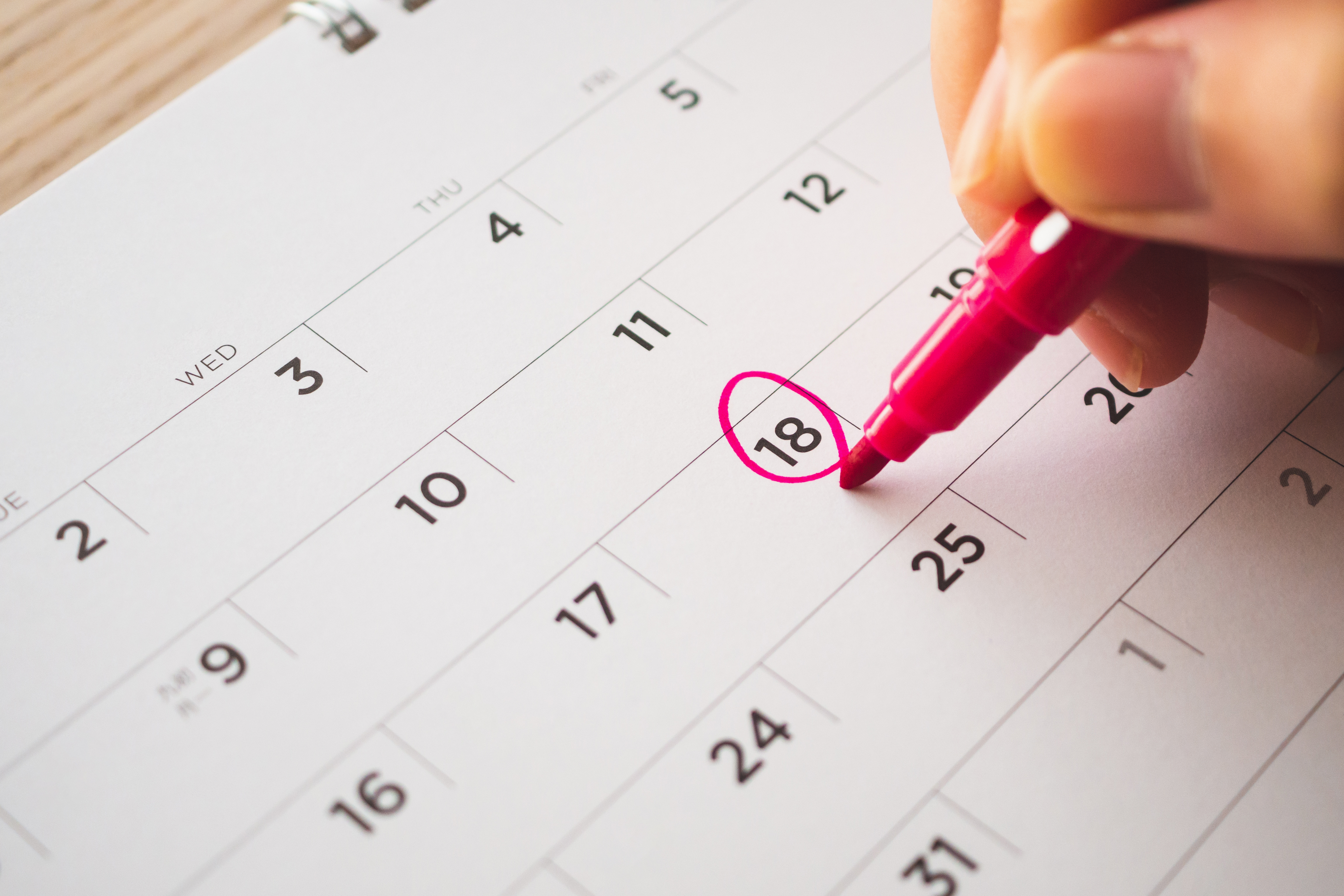 Woman’s hand with pink pen mark on calendar date