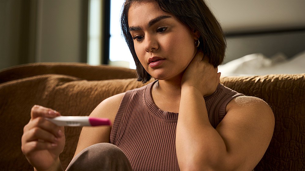 A woman sitting on the floor, looking unsettled as she gazes at the results of a pregnancy test.