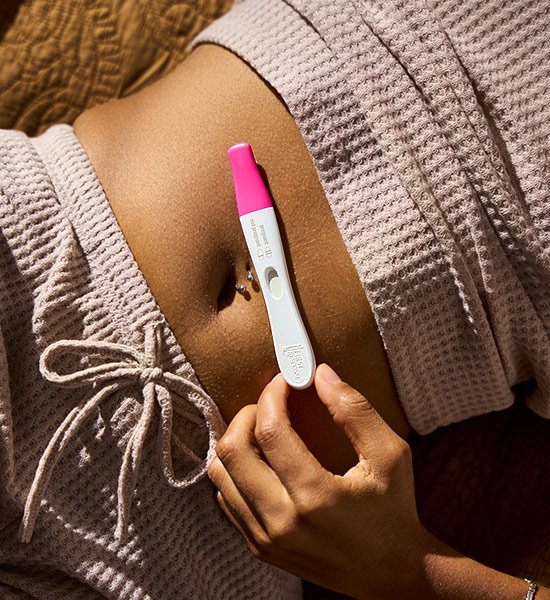 Woman holding a First Response pregnancy test up to her stomach.