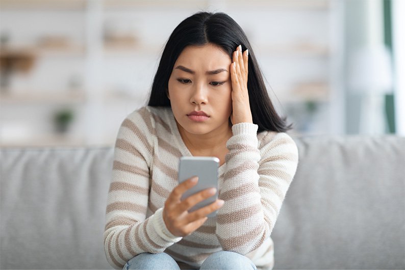 Woman sitting on couch with a worried expression researching on her smartphone.